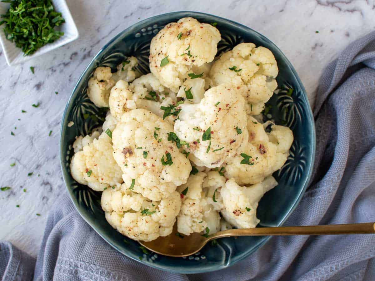 Finished cauliflower recipe in a blue bowl on a table, viewed from above.