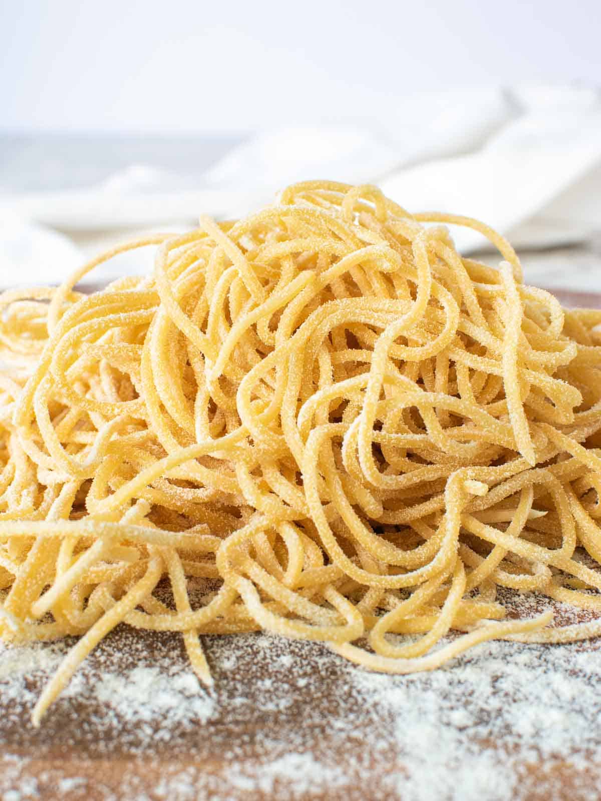 A pile of yellow homemade tonnarelli pasta on a wooden board.