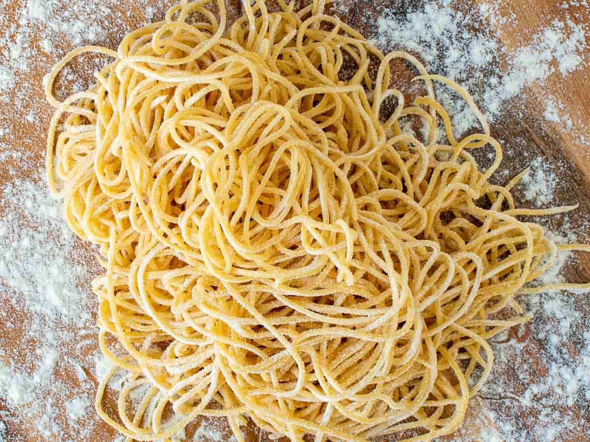 A pile of homemade tonnarelli pasta on a wooden board viewed from above.