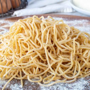 pile of yellow homemade spaghetti on wooden board.