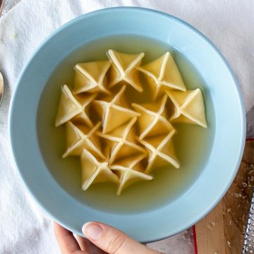 Pyramid shaped filled pasta in broth in blue bowl viewed from above.