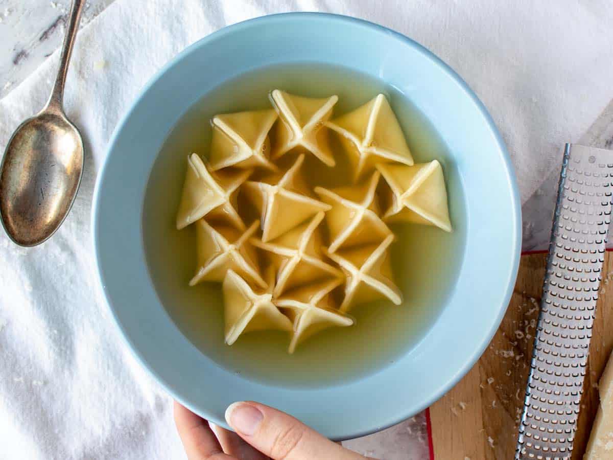 pyramid shaped filled pasta in broth in blue bowl viewed from above.