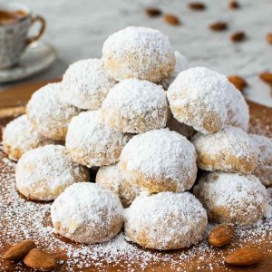 pile of white sugar coated cookies on wooden board with espresso cup in the background.