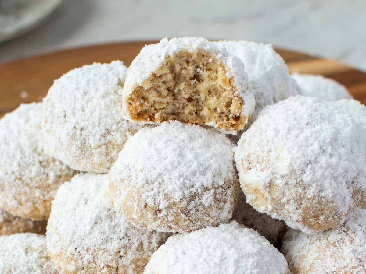 Pile of white sugar coated cookies, one cookie at the top with a bite taken out.