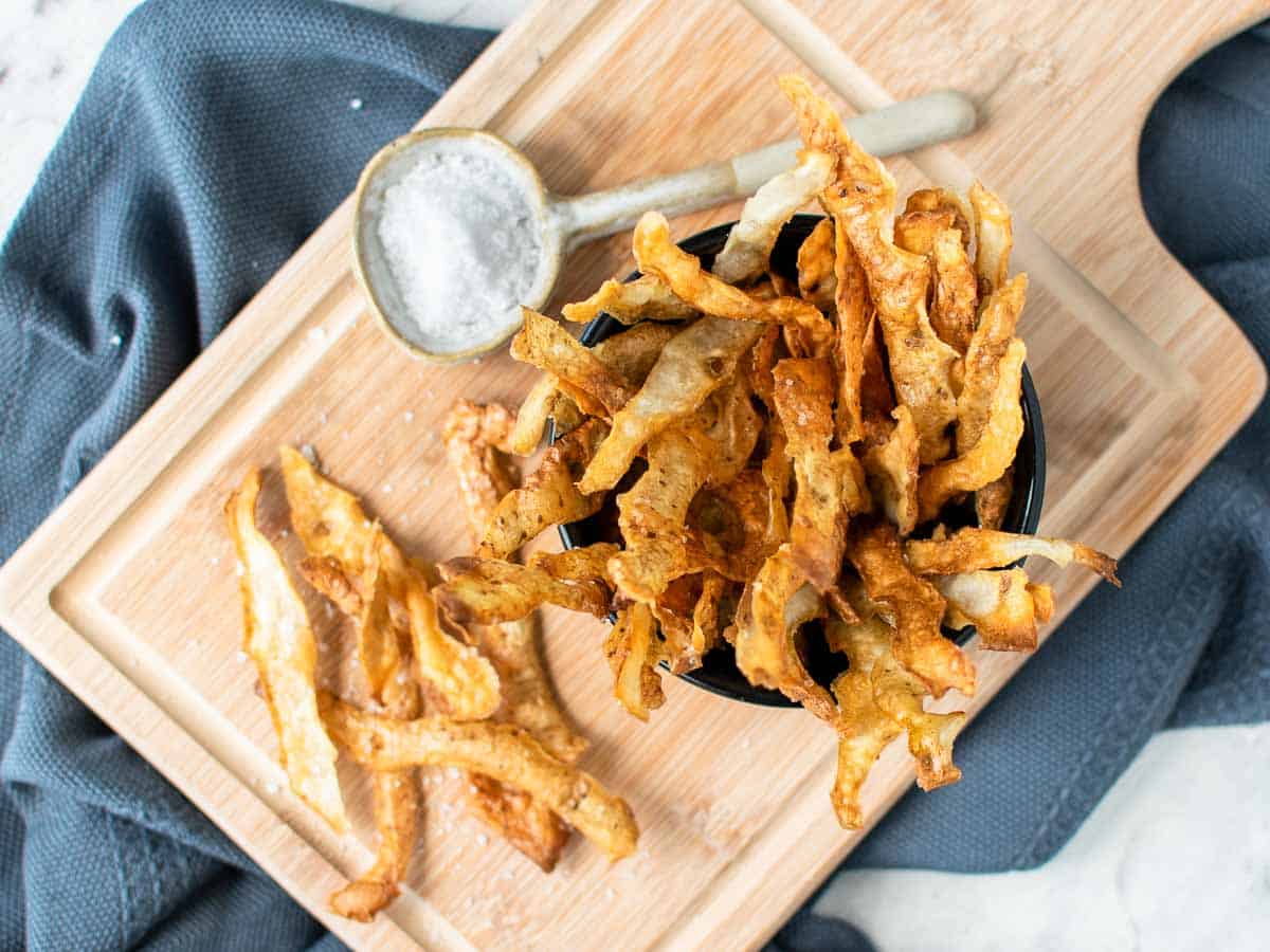 potato skin chips in black bowl on wooden board viewed from above.