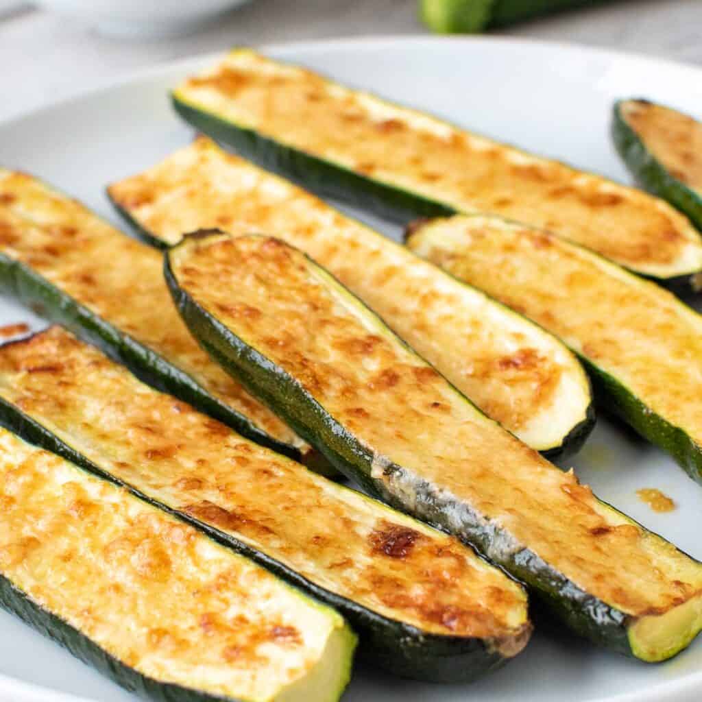 Pile of cheese topped zucchini on a white plate.