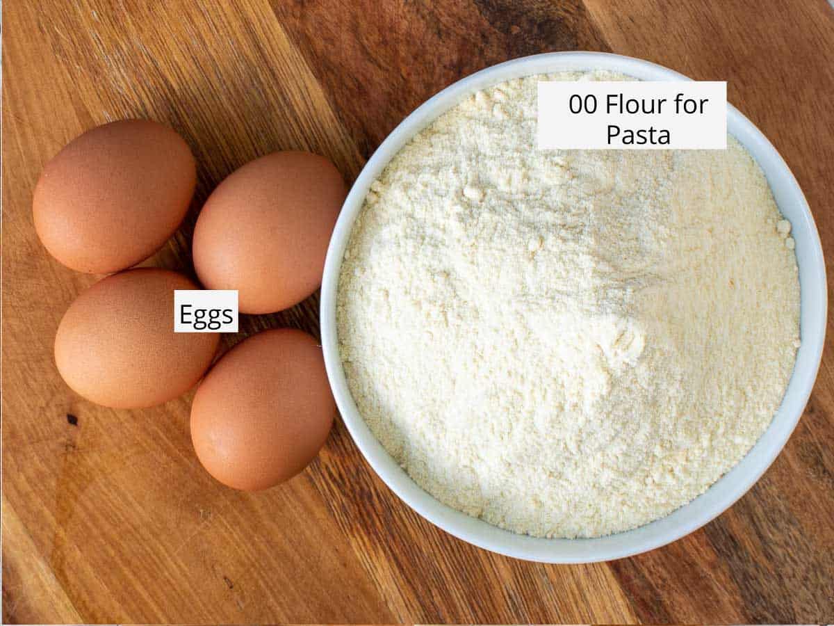 White bowl of flour and 4 eggs on wooden table viewed from above.