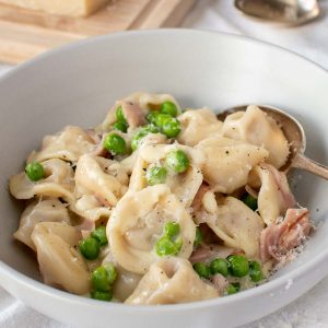 bowl of tortellini with peas and ham.