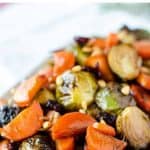 image with text. text reads 'holiday side dish roasted carrots and brussels sprouts". image is roasted carrots and brussel sprouts on white oblong plate.