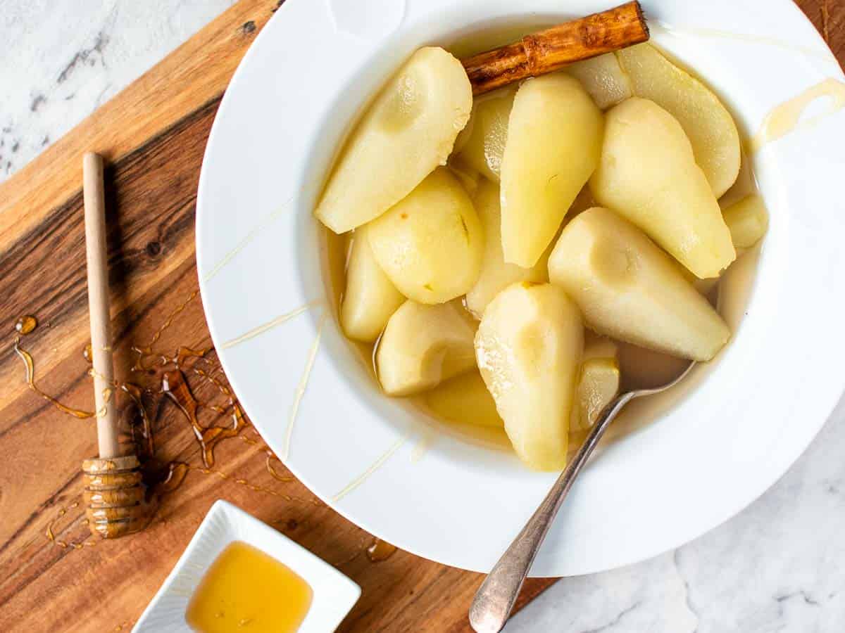 cooked peeled and quartered pears in a white large rimmed bowl with spoon viewed from above.