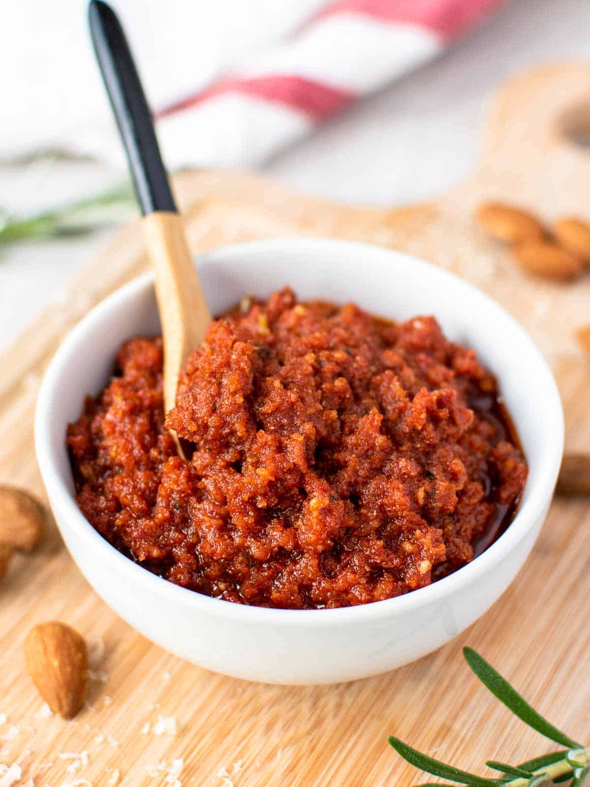 sun dried tomato pesto in a white bowl with small wooden spoon in the pesto.