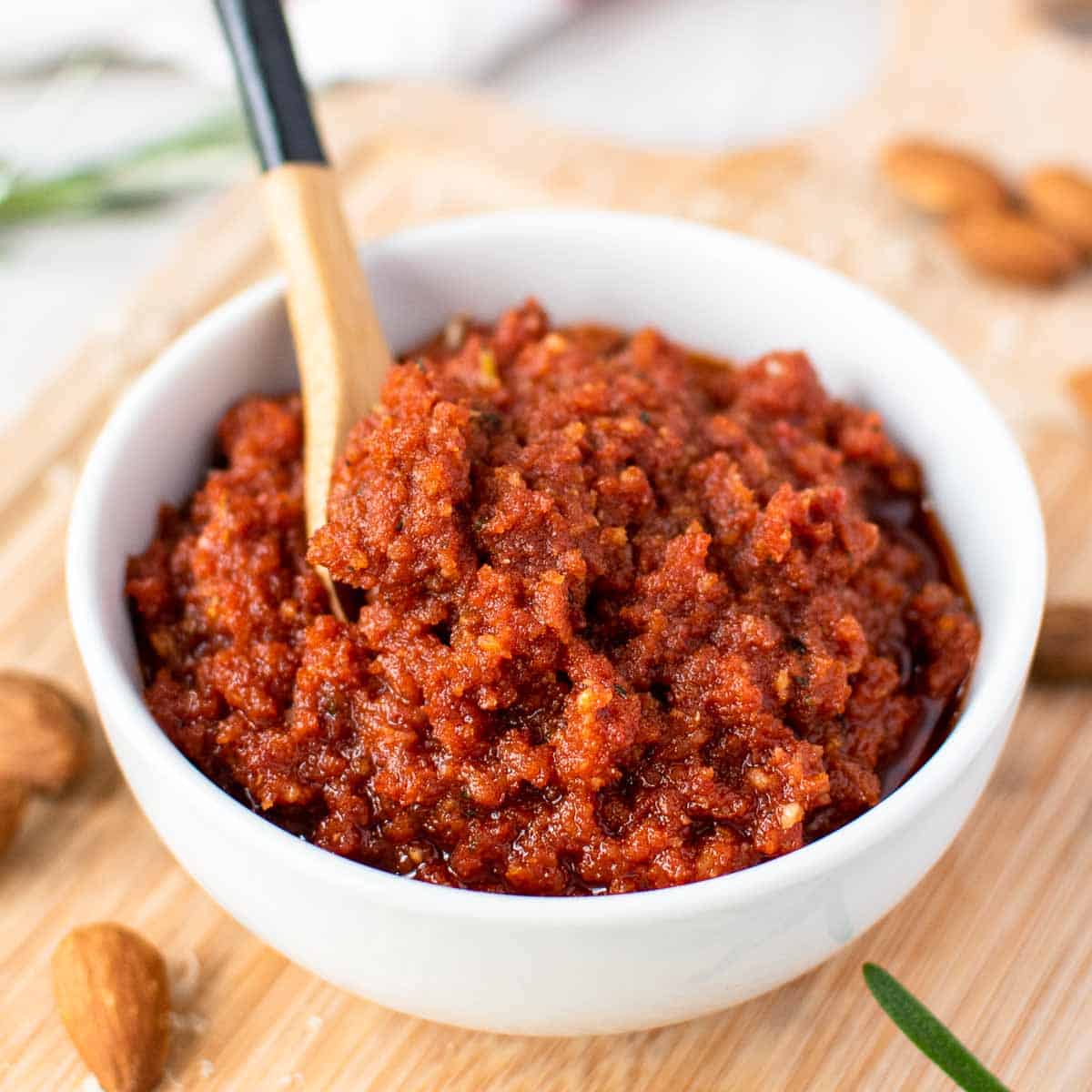 sun dried tomato pesto in a white bowl with small wooden spoon in the pesto.