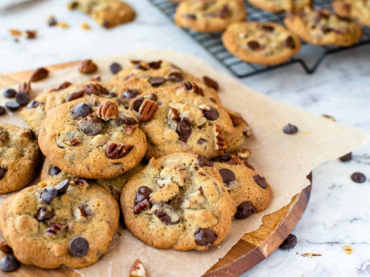 cookies on a wooden board that's covered in paper with more on a black wire cooling rack.