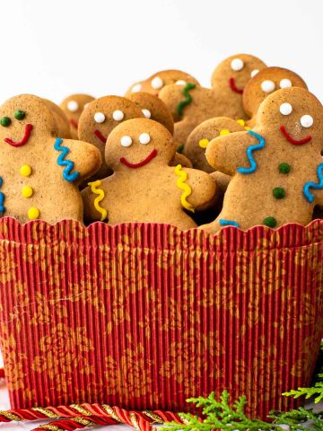 gingerbread people in red box surrounded by green leaves and red cord.