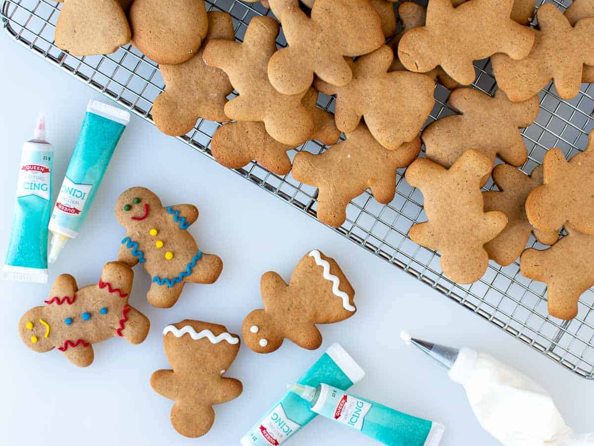 Gingerbread people on black wire rack with some decorated cookies and icing supplies nearby.