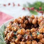 italian honey balls piled into a wreath shape on a white plate with green rosemary sprigs all around it.