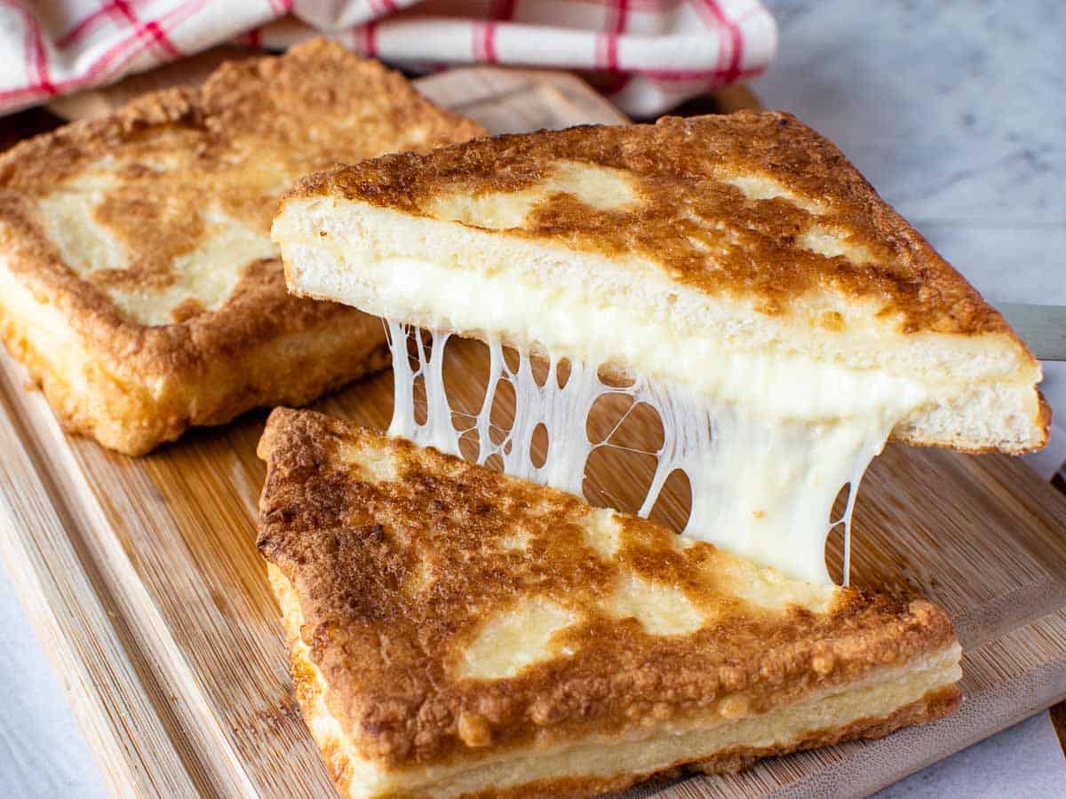 fried cheese sandwich cut in half and showing cheese pull with second sandwich in background.