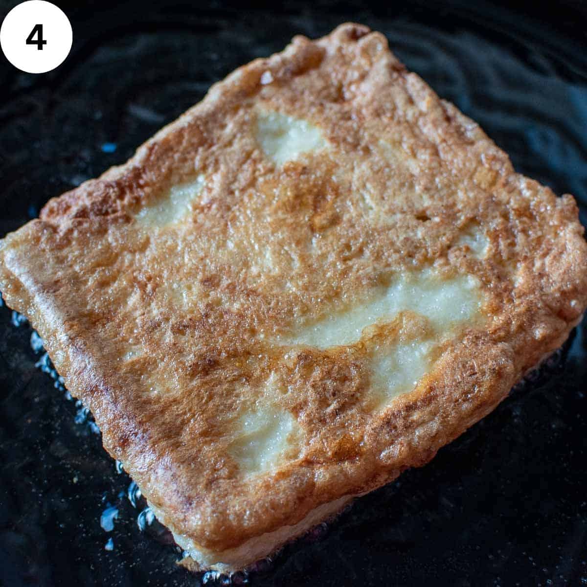 Sandwich of eggy bread frying in oil in a skillet.