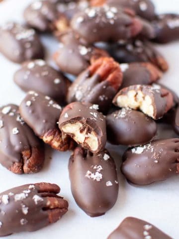 Close up of two dozen chocolate covered pecans sprinkled with flaked salt and resting on white parchment paper.