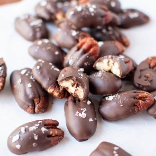 Close up of two dozen chocolate covered pecans sprinkled with flaked salt and resting on white parchment paper.