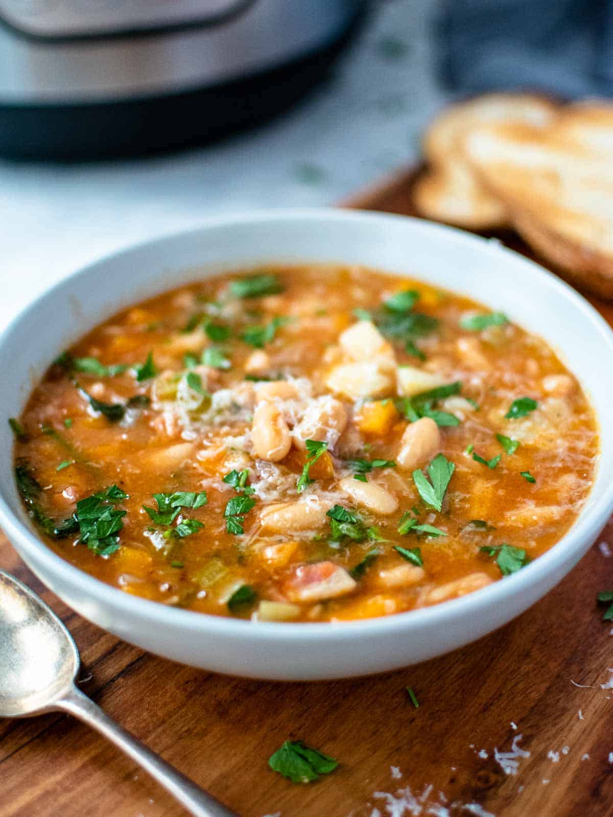 instant pot cannellini bean soup in a pale blue bowl on wooden board.