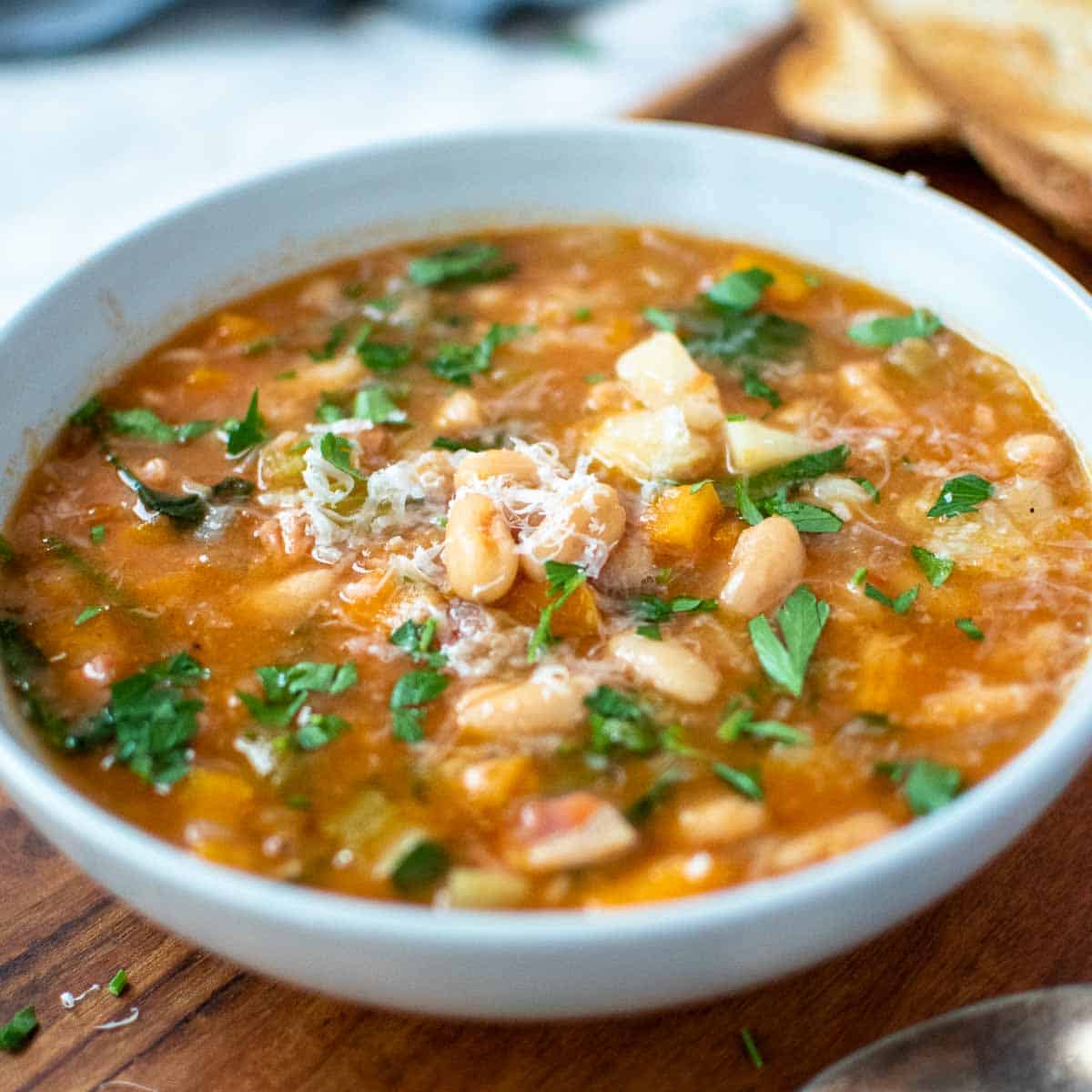 instant pot cannellini bean soup in a pale blue bowl on wooden board.