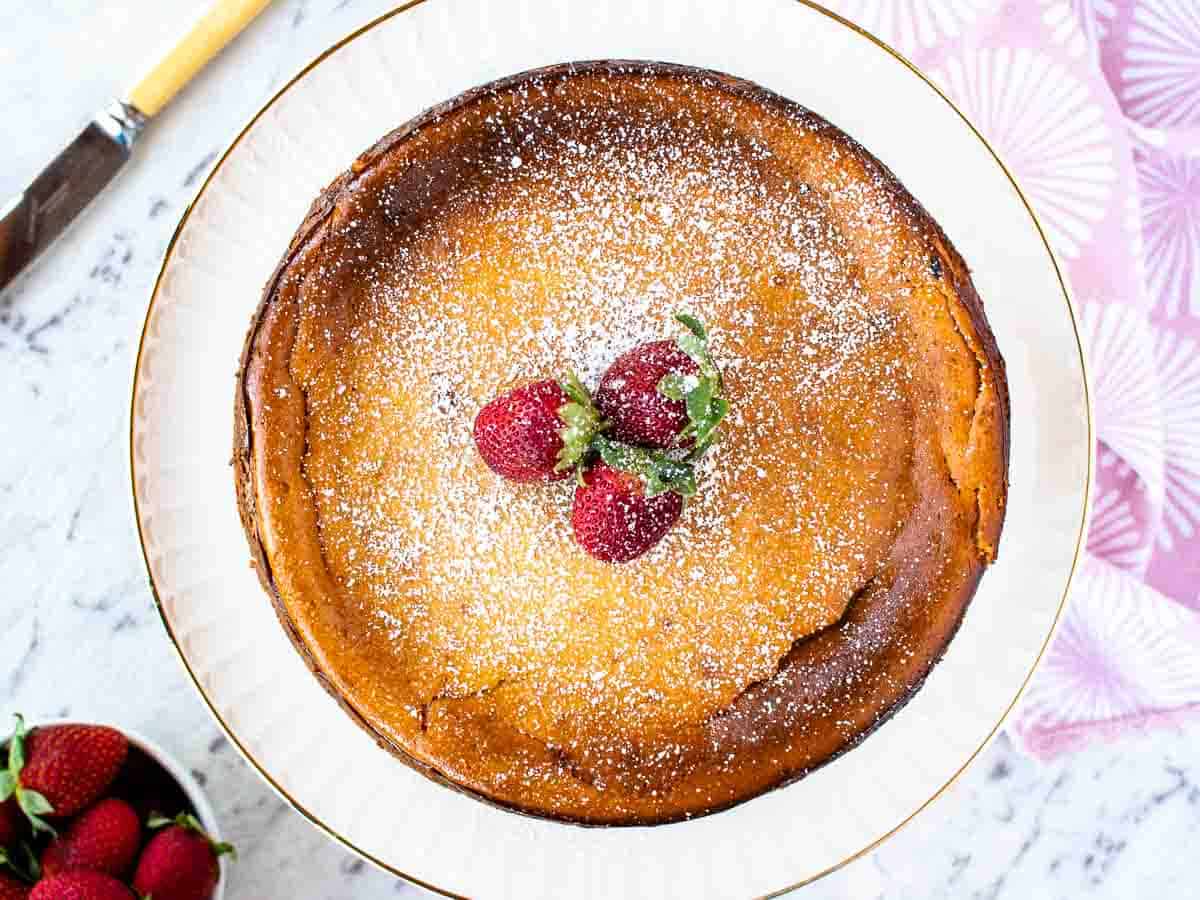 golden brown ricotta cheesecake with 3 strawberries on top viewed from above.