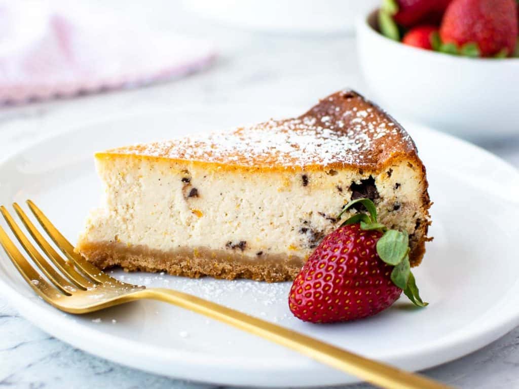 close up of a slice of sweet ricotta tart on white plate with a strawberry on the side.