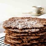 image with text. text reads 'easy italian classic chocolate pizzelle'. image is stack of chocolate wafer cookies on black wire rack.