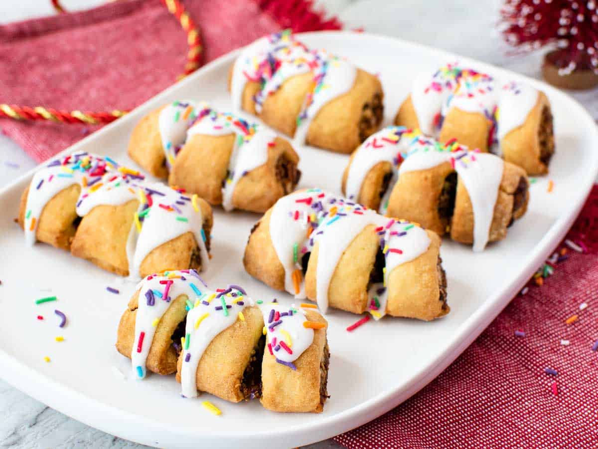 seven cookies with slits revealing dark filling drizzled with white icing and colored sprinkles on a white oblong plate.