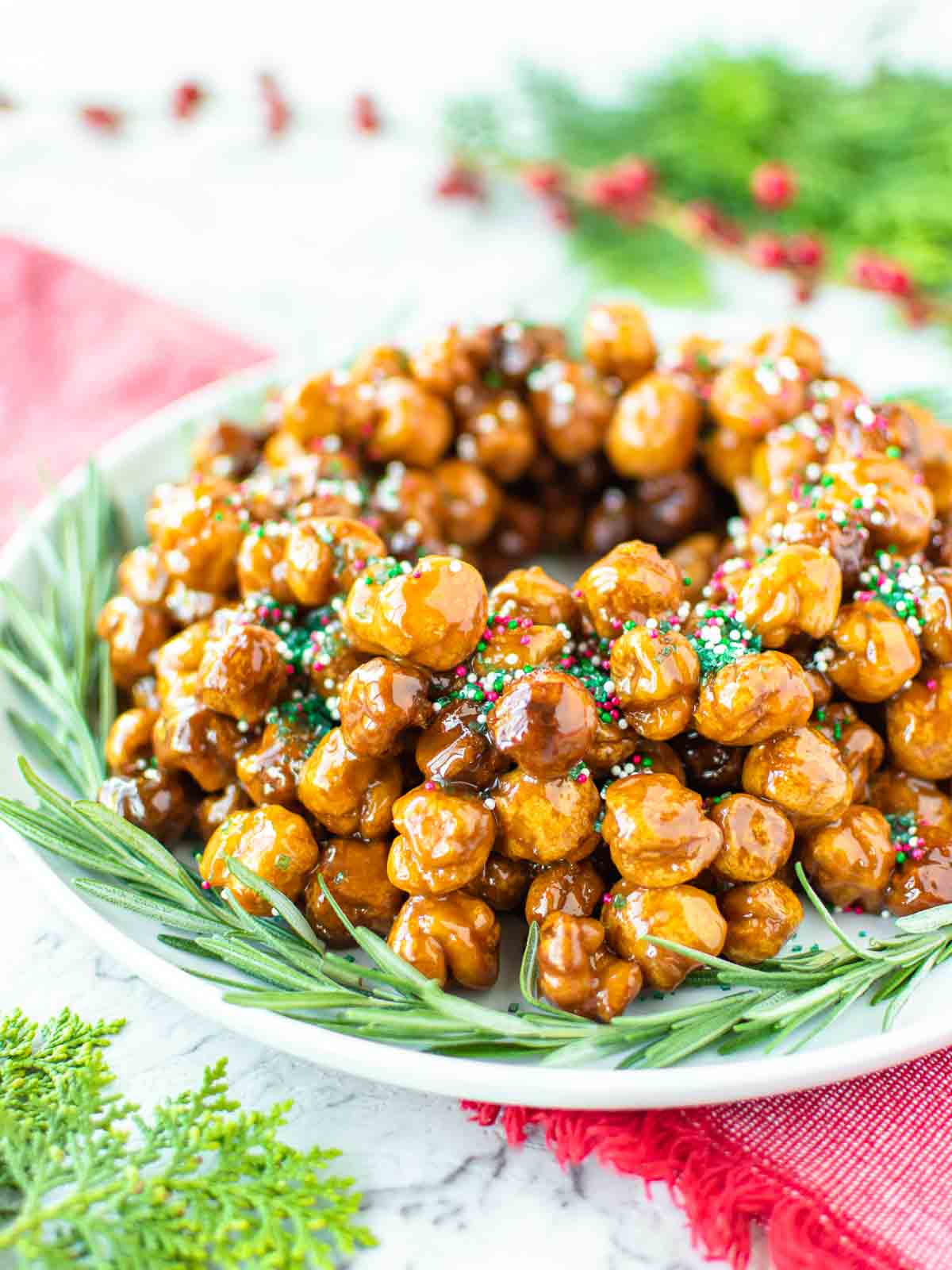 italian honey balls piled into a wreath shape on a white plate with green rosemary sprigs all around it.