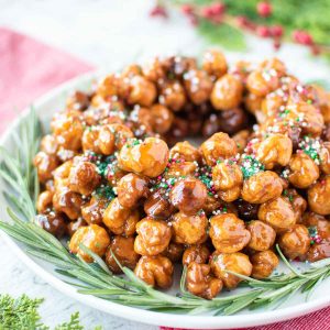 italian honey balls piled into a wreath shape on a white plate with green rosemary sprigs all around it.