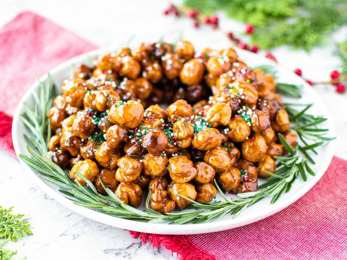 golden brown fried dough balls coated in honey piled onto a white plate in the shape of a wreath.
