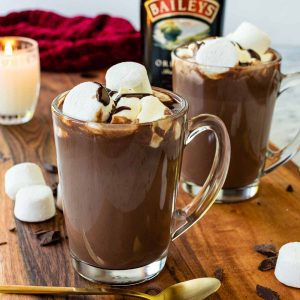 two mugs of hot chocolate with bottle of baileys irish cream in the background.