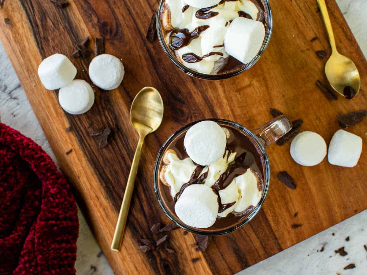 A top down view of mugs of hot chocolate served with cream and marshmallows.