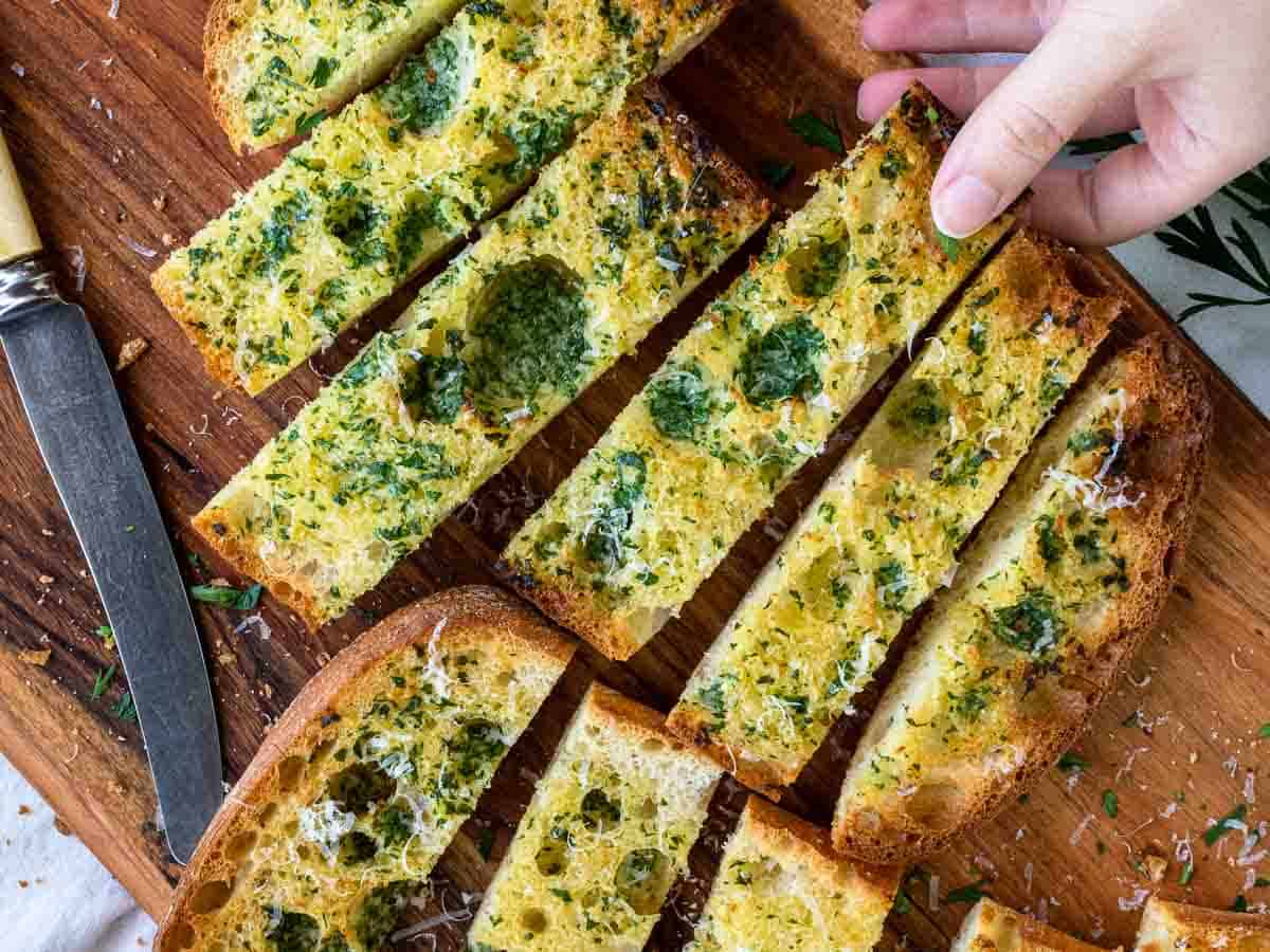 Slices of herby toasted ciabatta bread showing fingers taking a slice viewed from above.