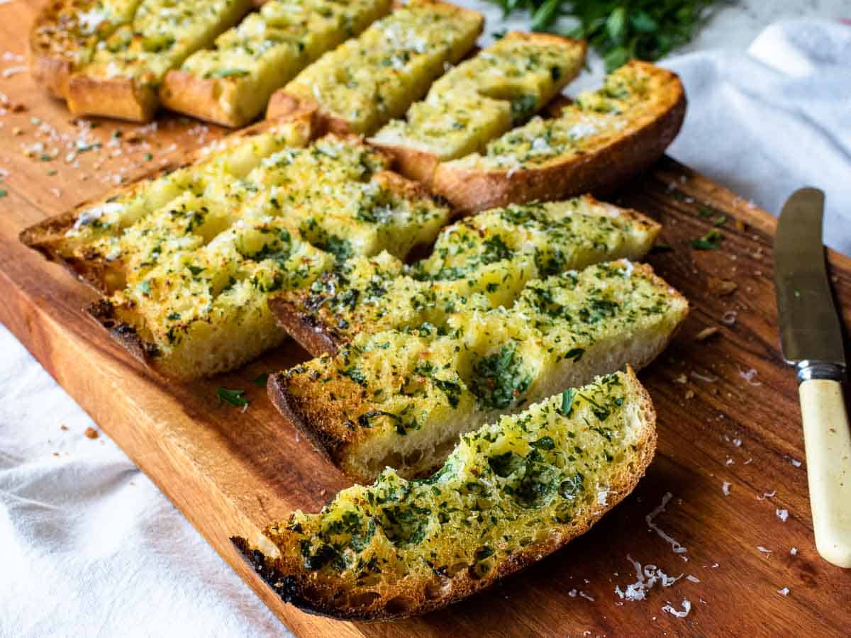 Slices of toasted ciabatta with chopped green herbs on top on a wooden board.