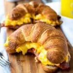 two croissants filled with scrambled egg on a wooden board.