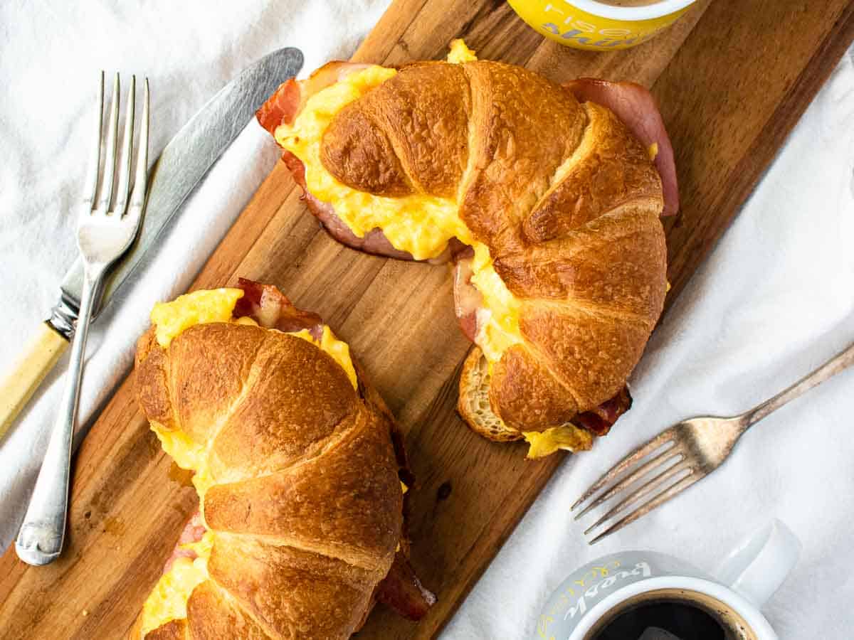 Croissants filled with eggs and bacon on a wooden board viewed from above.