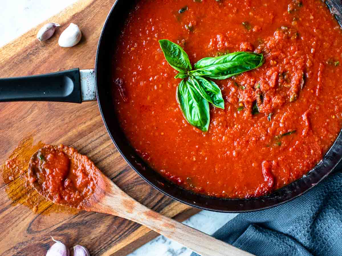 Overhead view of tomato sauce in a black skillet with basil sprig in the middle of the sauce.