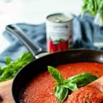 image with text. text reads 'classic Italian sauce san marzano tomato sauce'. image is tomato sauce in a black skillet with a sprig of basil in the centre.