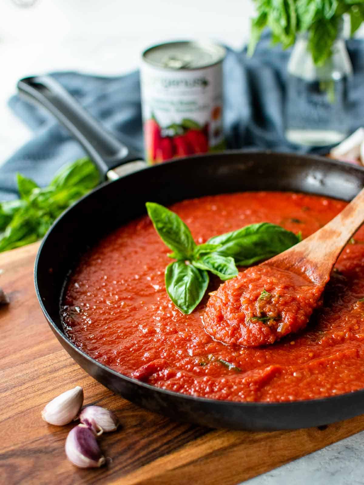 San Marzano tomato sauce in a black skillet with a sprig of basil in the centre.