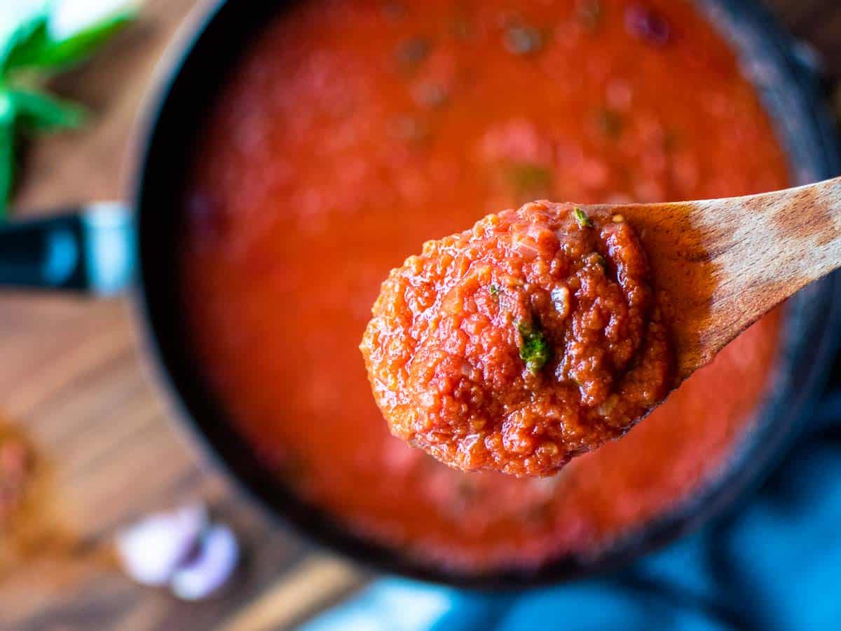 Close up of a spoonful of tomato sauce with the pan in the background.