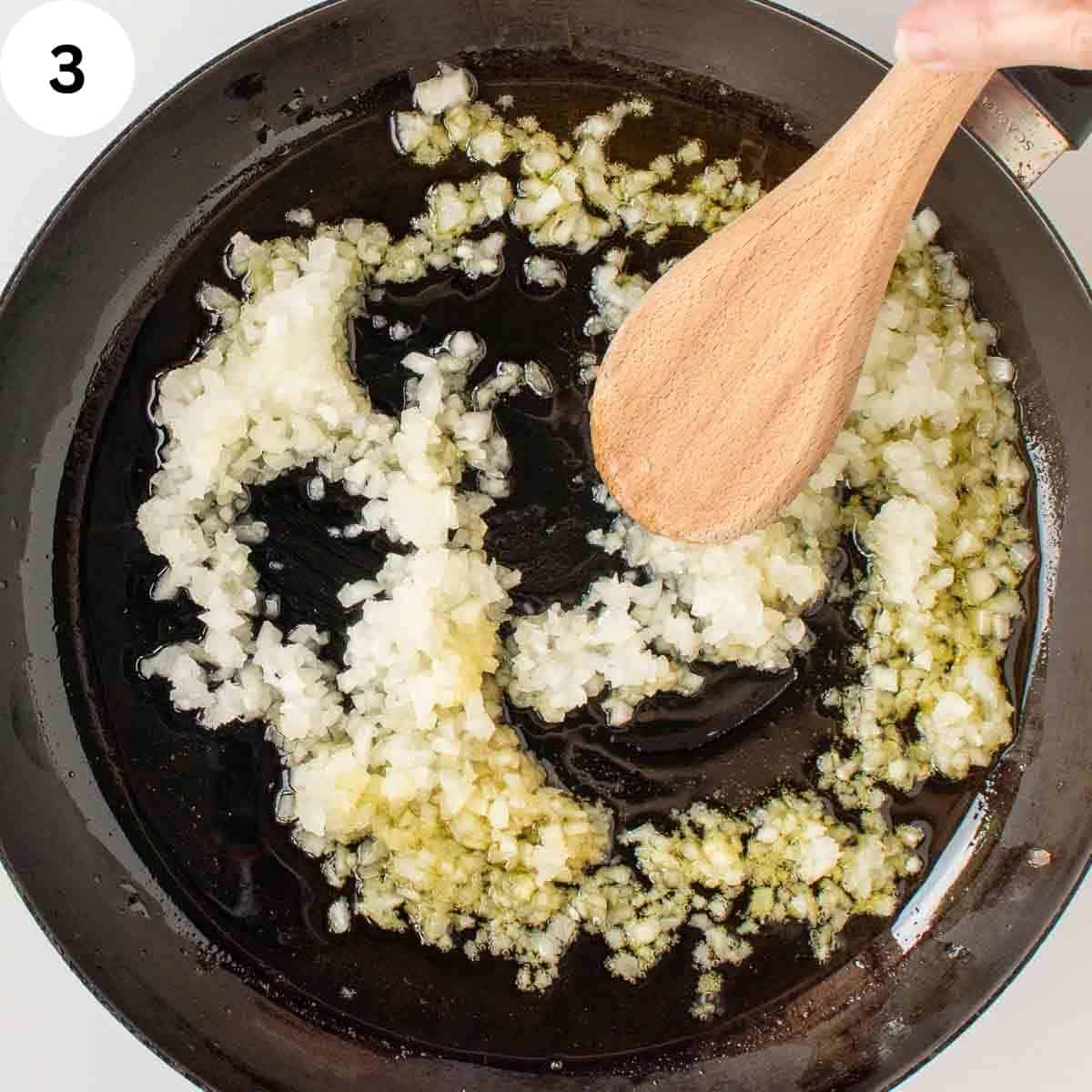 Finely chopped onion being stirred in a skillet with wooden spoon.