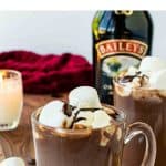 image with text. text reads 'boozy and delicious baileys hot chocolate'. image is two mugs of hot chocolate with bottle of baileys irish cream in the background.