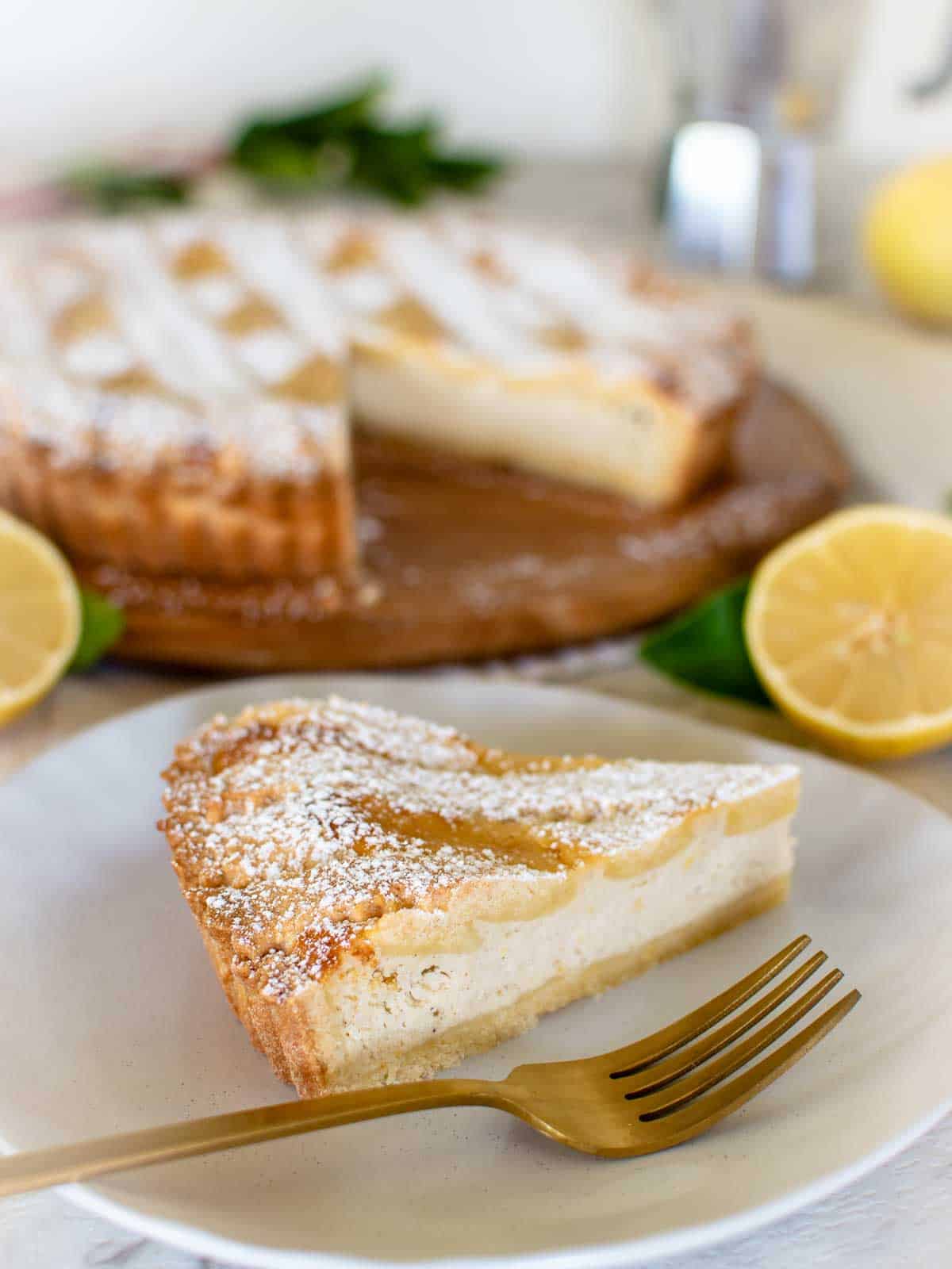 Slice of ricotta pie on white plate with gold fork and whole pie in the background.