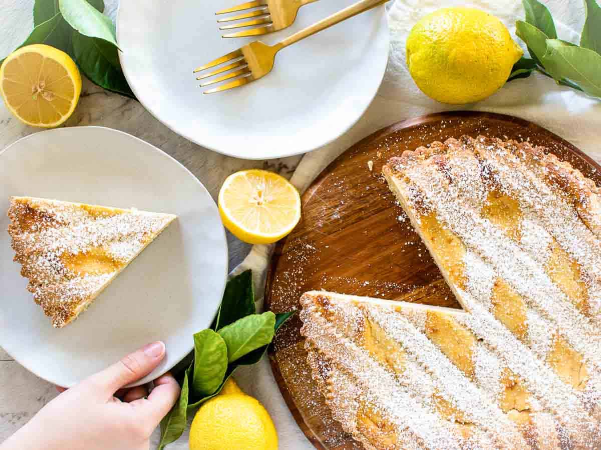 Overhead view of latticed topped pie, a slice of pie, white plates, lemons and lemon leaves.