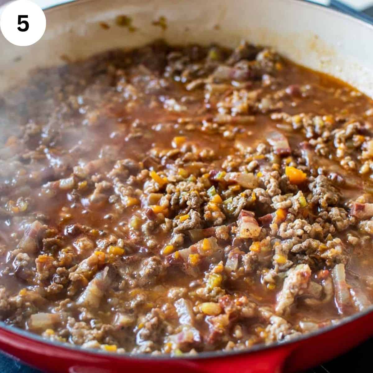 Ground meat simmering in sauce in a round pan.