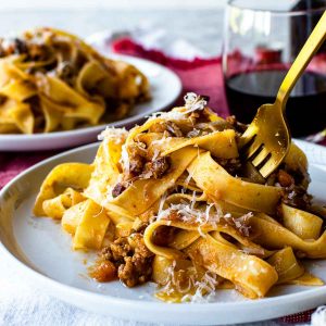 white plate with pasta on it and a gold fork in the pasta.