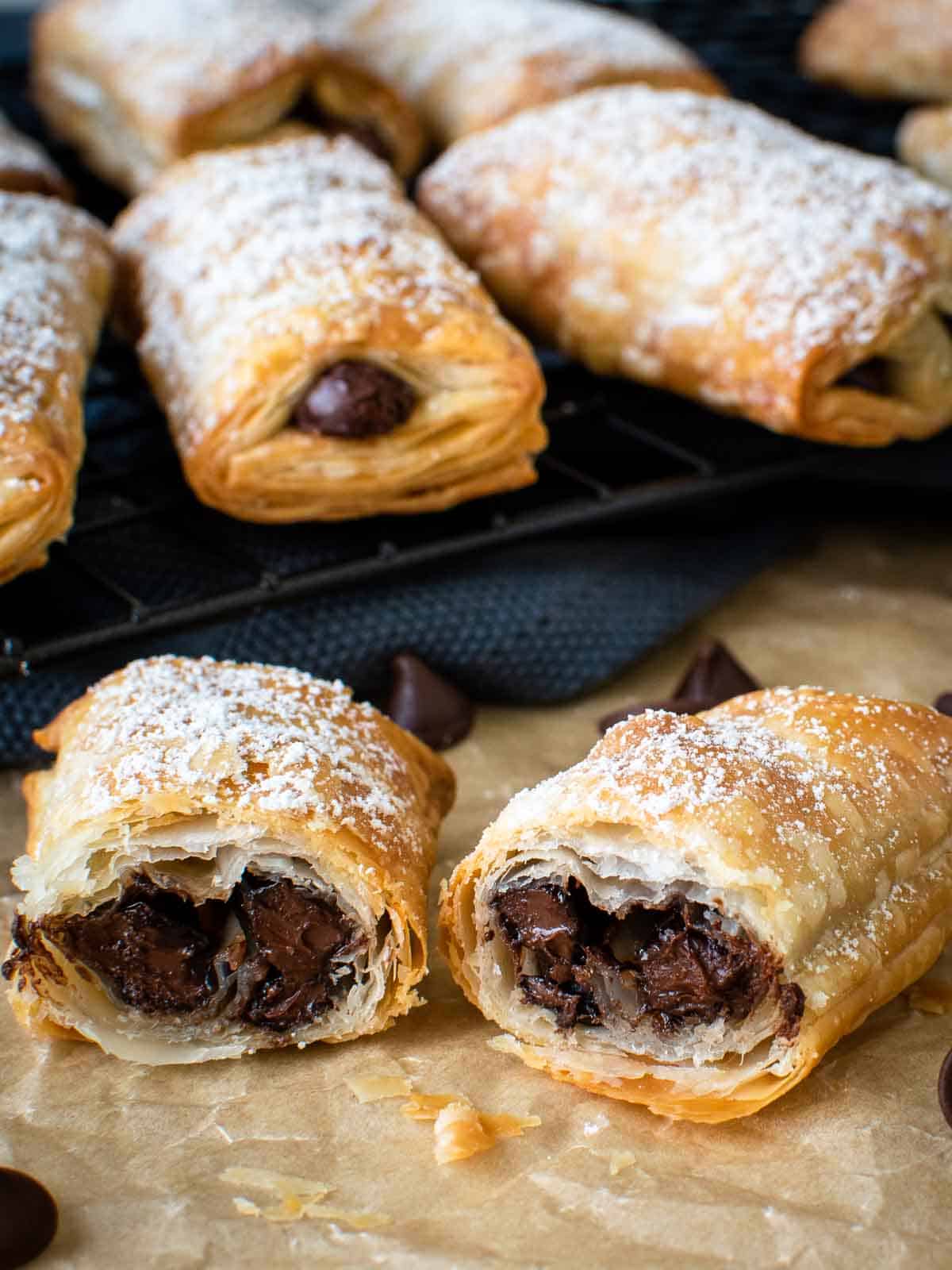 Crispy puff pastry rolls cut in half showing with chocolate in the centre, more in the background.